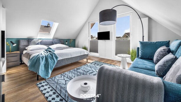 A modern loft bedroom with a bed, a sofa, a coffee table, and a large window. - Ferienhaus Meerglück (Büsum)