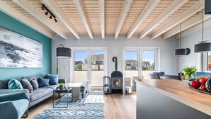 Una sala moderna con sofá, mesa de centro y chimenea. Dos puertas dan acceso a un balcón con vistas a casas.