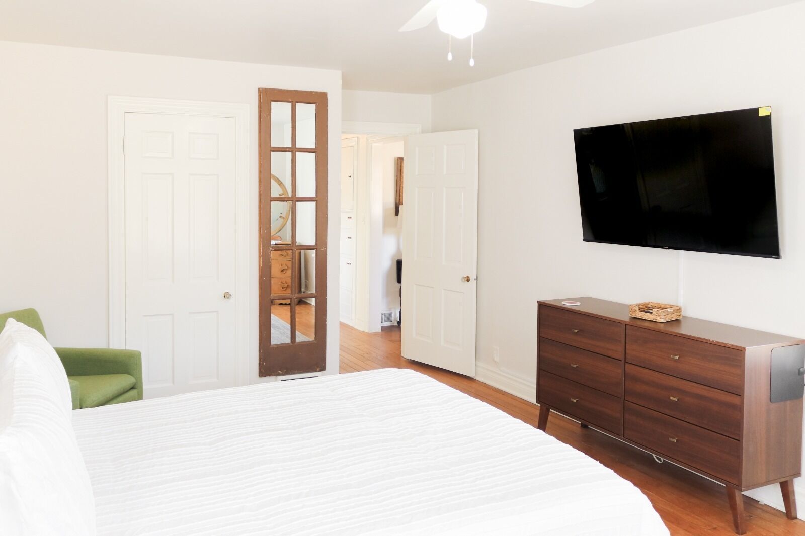 Un dormitorio con cama, cómoda, televisor y una silla verde.