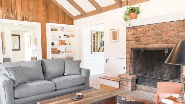 A living room with a grey sofa, a wooden coffee table, a fireplace, and a bookshelf with various items.