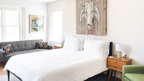 A bedroom with a large bed, a grey sofa, a green armchair, and a wooden wall art piece.