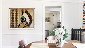 A dining area with a wooden table, striped placemats, a vase with flowers, and a wall-mounted painting.