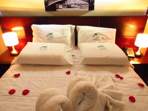 Habitación de hotel con cama, dos almohadas, televisión en la pared y mesita de noche con lámpara y teléfono.
