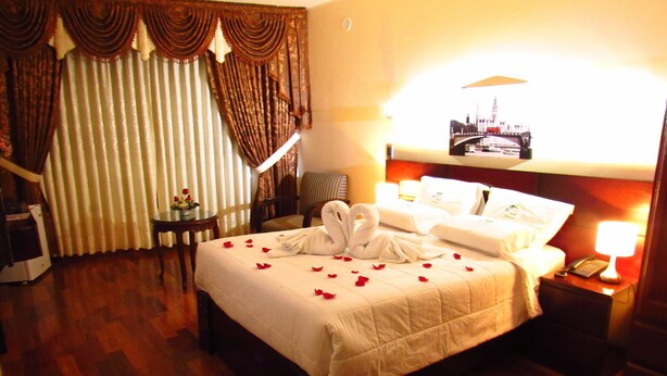 Una habitación de hotel con una cama grande, una mesita de noche con lámpara, una silla y cortinas.