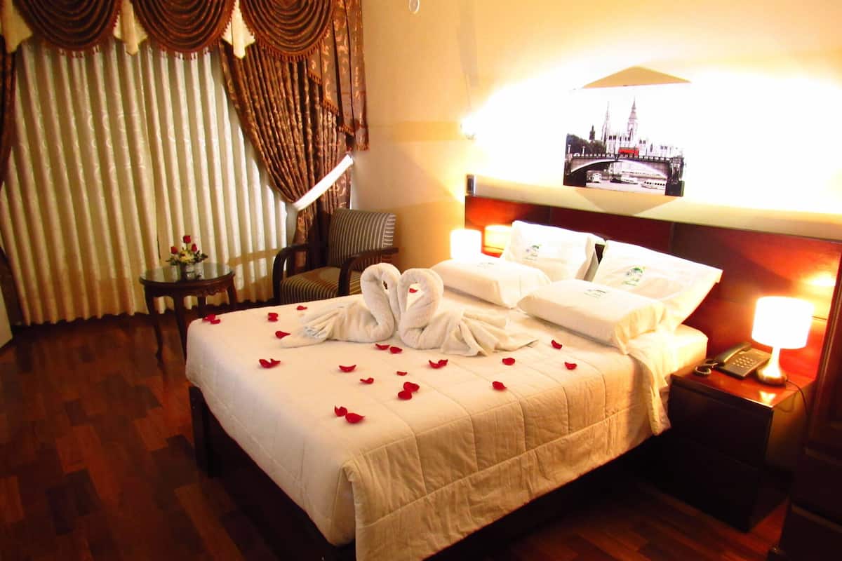 A hotel room with a large bed, a bedside table with a lamp, a chair, and a picture on the wall.