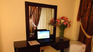 Una habitación compacta con una laptop sobre un escritorio, un refrigerador pequeño y un florero con flores.