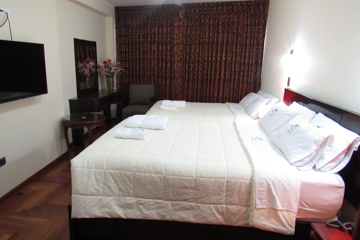 A hotel room with a large bed, a flat-screen TV, a desk, and a chair.