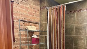 A bathroom with a white toilet, a wooden cabinet, a metal shelf with toiletries, and a shower curtain.