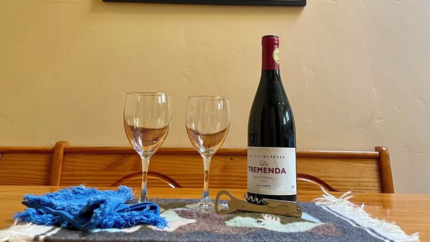 A table with two wine glasses, a bottle of wine, and a colorful abstract painting on the wall.
