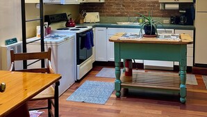 A kitchen with white cabinets, a wooden table, and a brick wall.