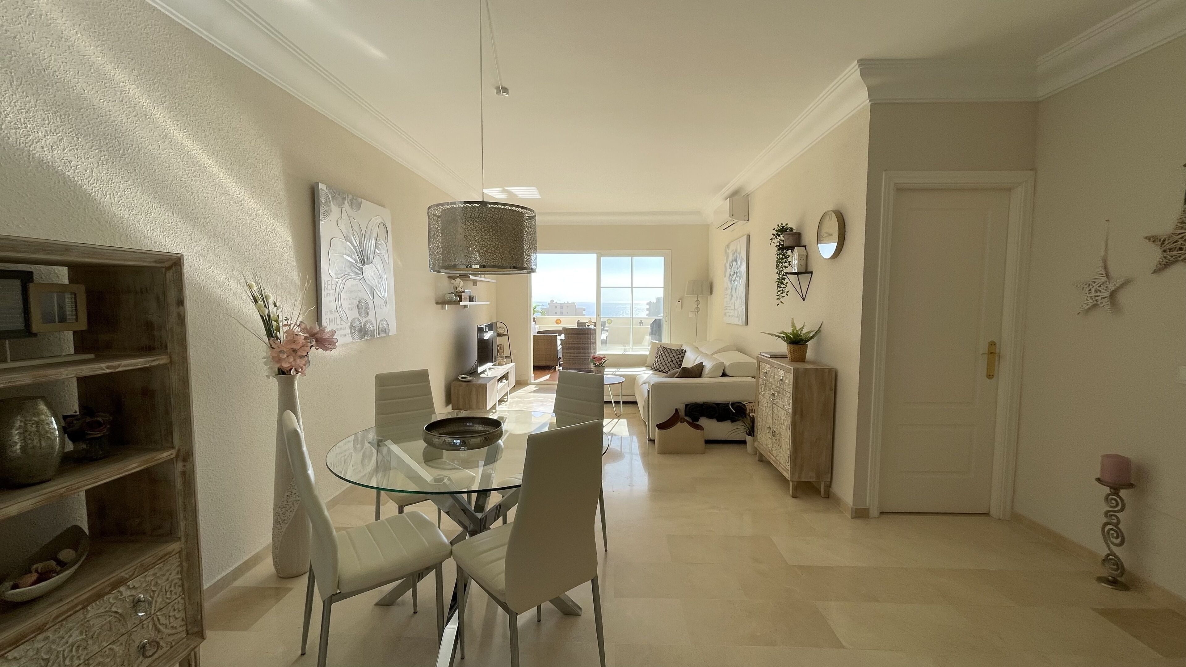 A spacious living area with a glass dining table, comfortable seating, a sofa, and a view of the outdoors.