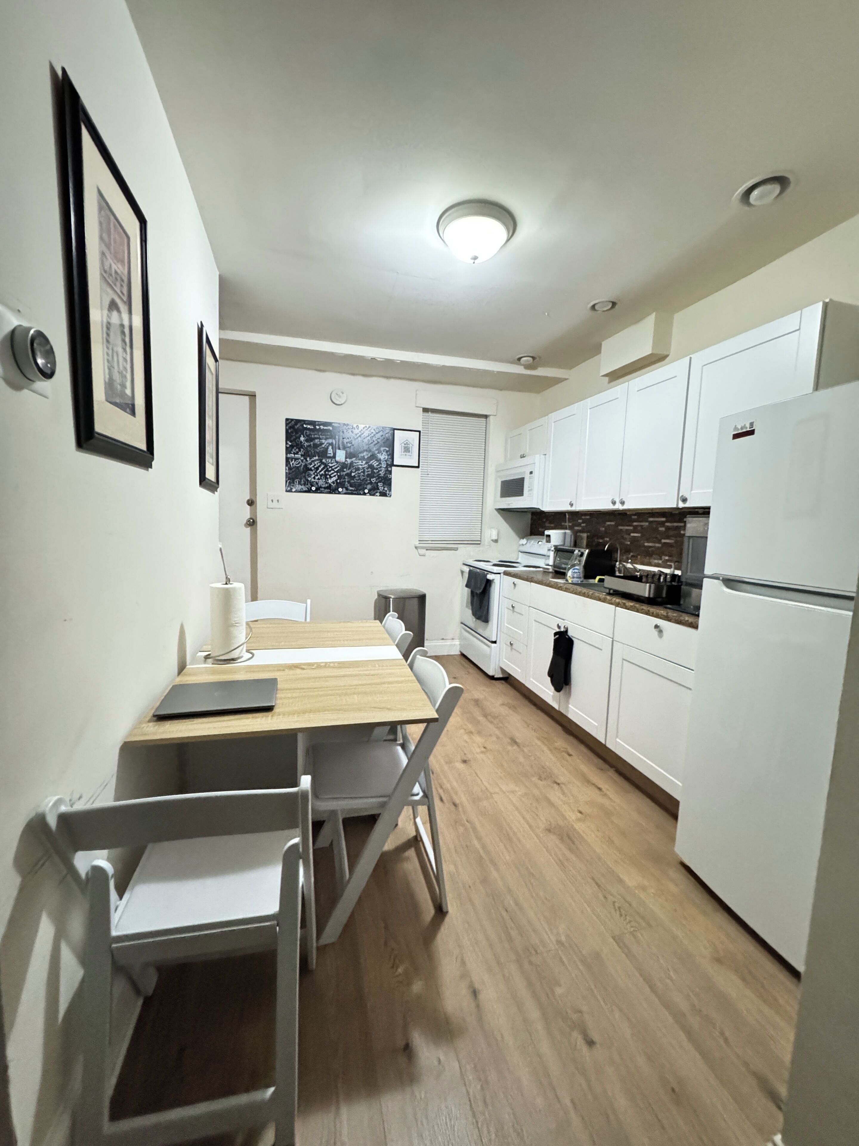 A compact kitchen with white cabinets, a wooden dining table, and a small window.