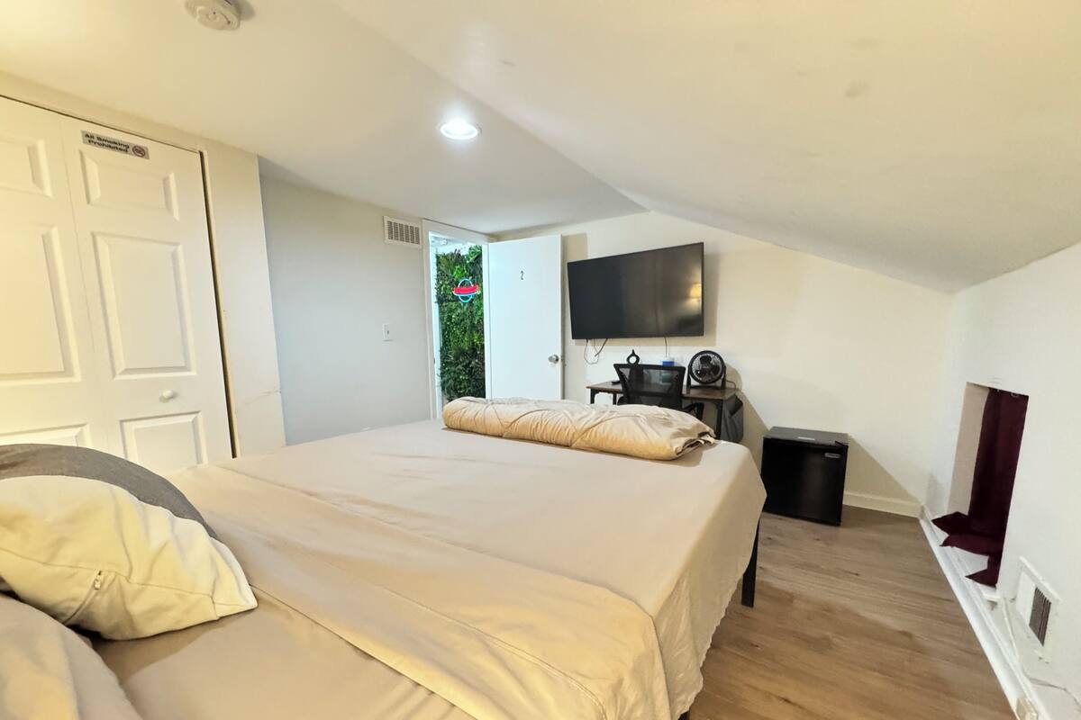 A bedroom with a bed, a desk, a TV, and a window.