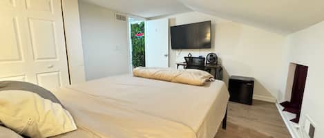 A bedroom with a bed, a desk, a TV, and a window.