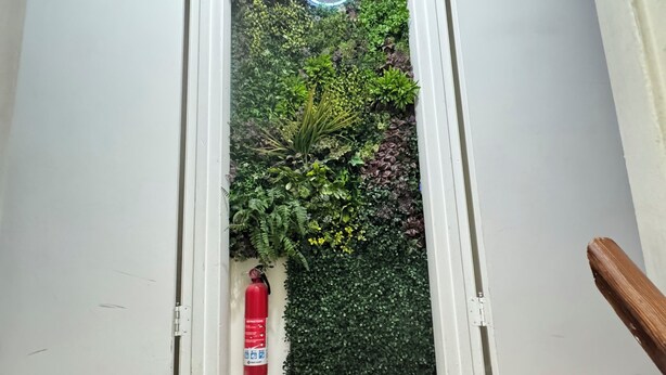 Un pasillo con pared de jardín vertical, un letrero de neón y un extintor.