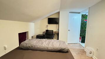 A bedroom with a bed, a desk with a chair, a TV on the wall, and a door leading to a balcony.