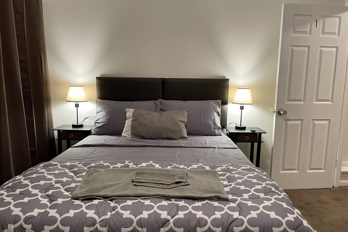 A neatly made bed with a patterned bedspread, two bedside lamps, and a door to the right.