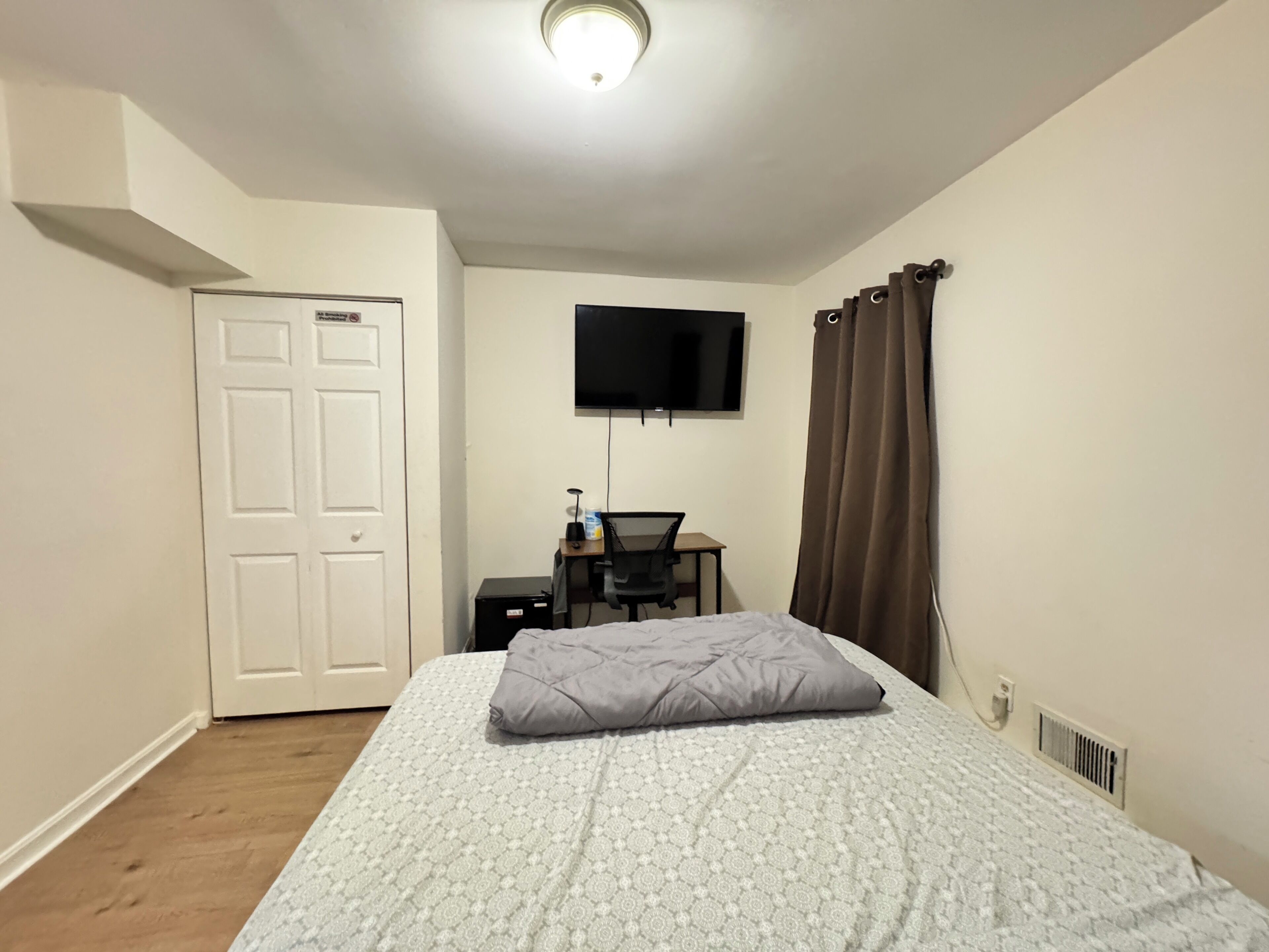 A bedroom with a bed, a desk, a chair, a television, and a door.