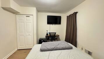 A bedroom with a bed, a desk, a chair, a television, and a door.