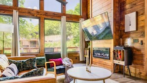 A cozy living room with a large window, a flat-screen TV, a fireplace, and a bookshelf. - King beds, quiet neighborhood. Hot tub, games & fire pit! 5 mi to Dollywd.  (Sevierville)