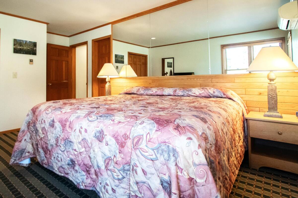 Ett hotellrum med en säng, ett träbeklätt sänggavel, två sänglampor, en byrå och en spegel på väggen.