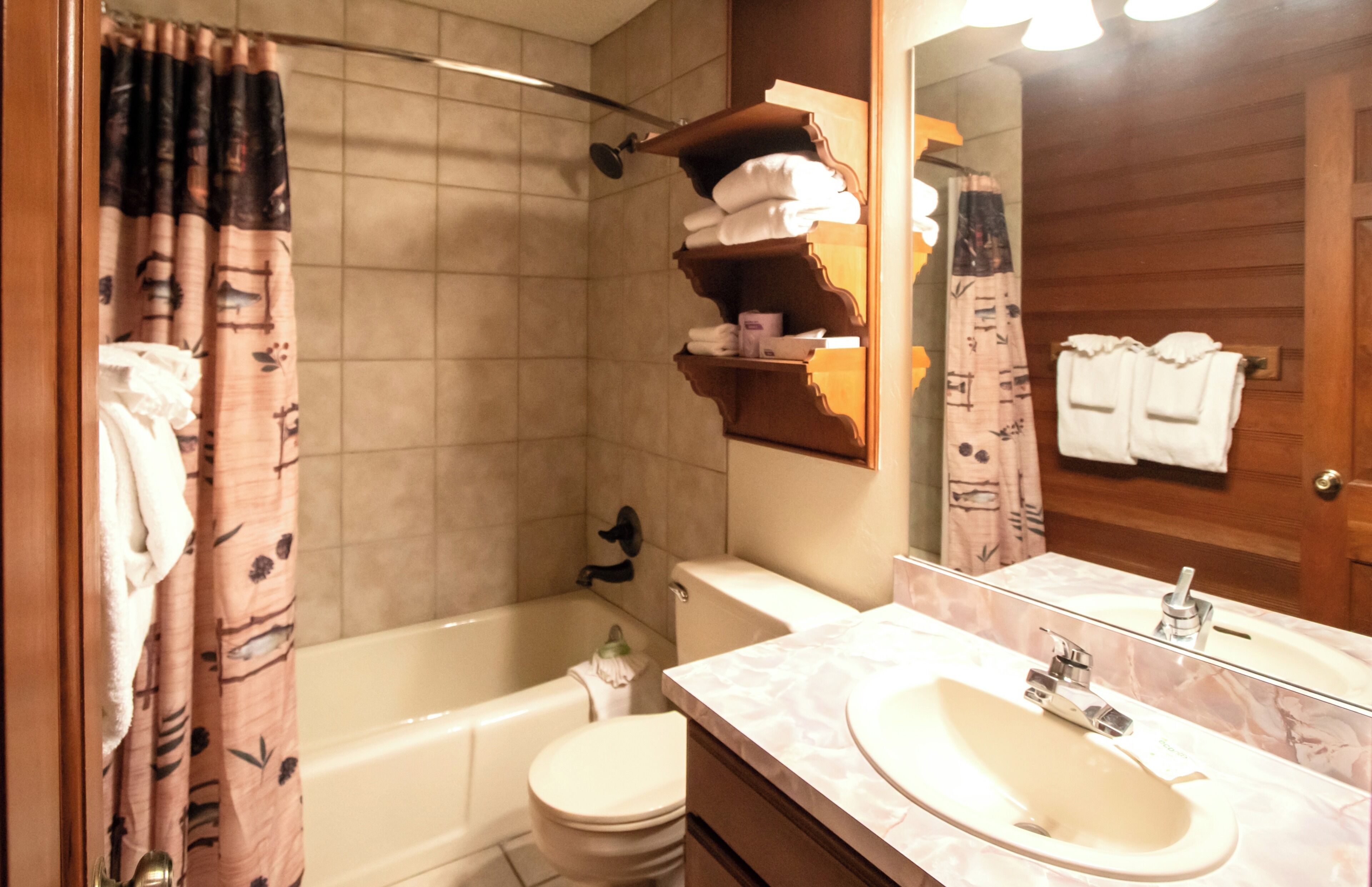 Un baño con bañera, inodoro y lavamanos. Hay toallas y artículos de aseo en las repisas.