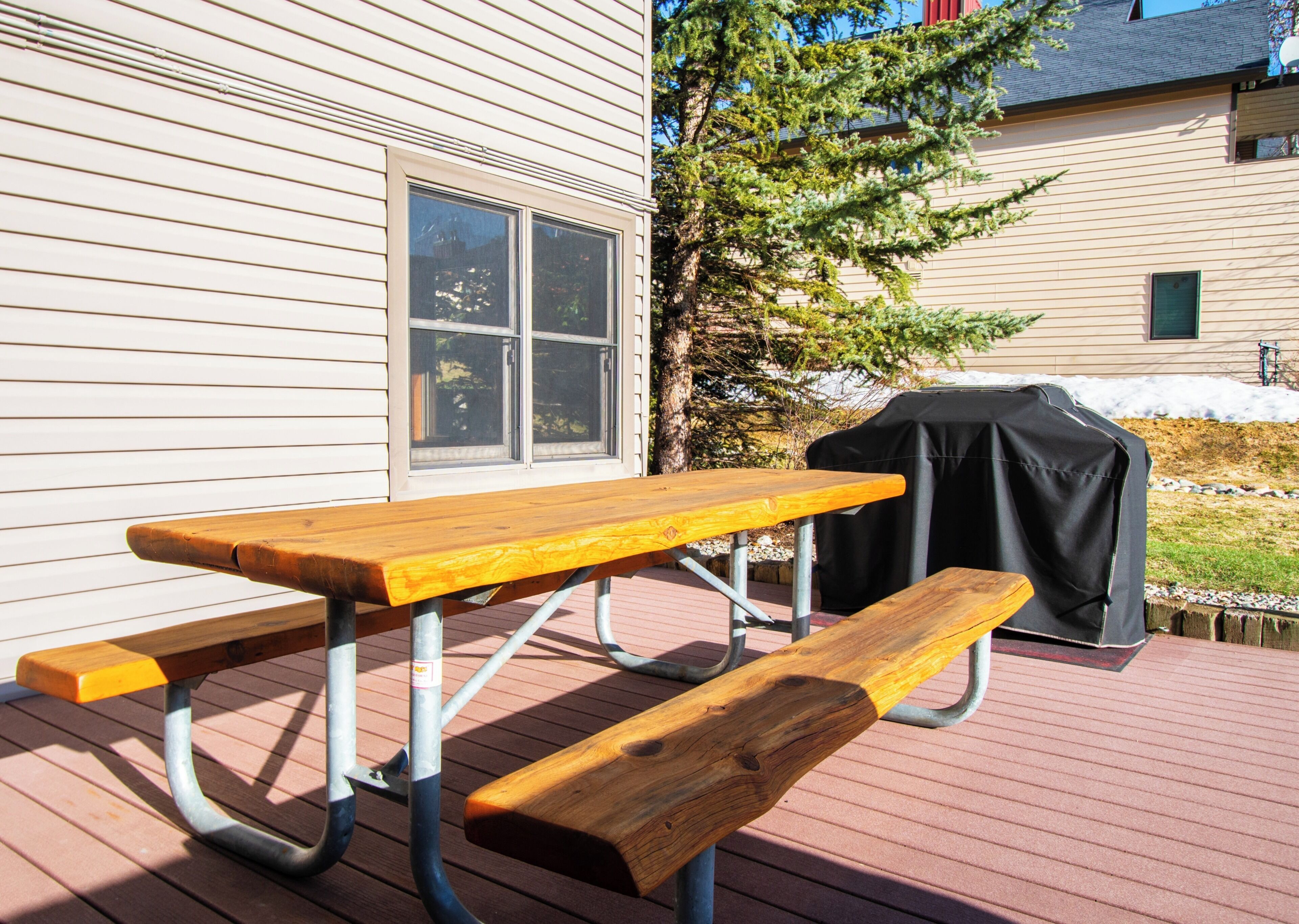 An outdoor picnic table with benches, a grill, and a house in the background.
