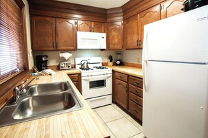 Una cocina con armarios de madera, estufa blanca, microondas, pileta y refrigerador.