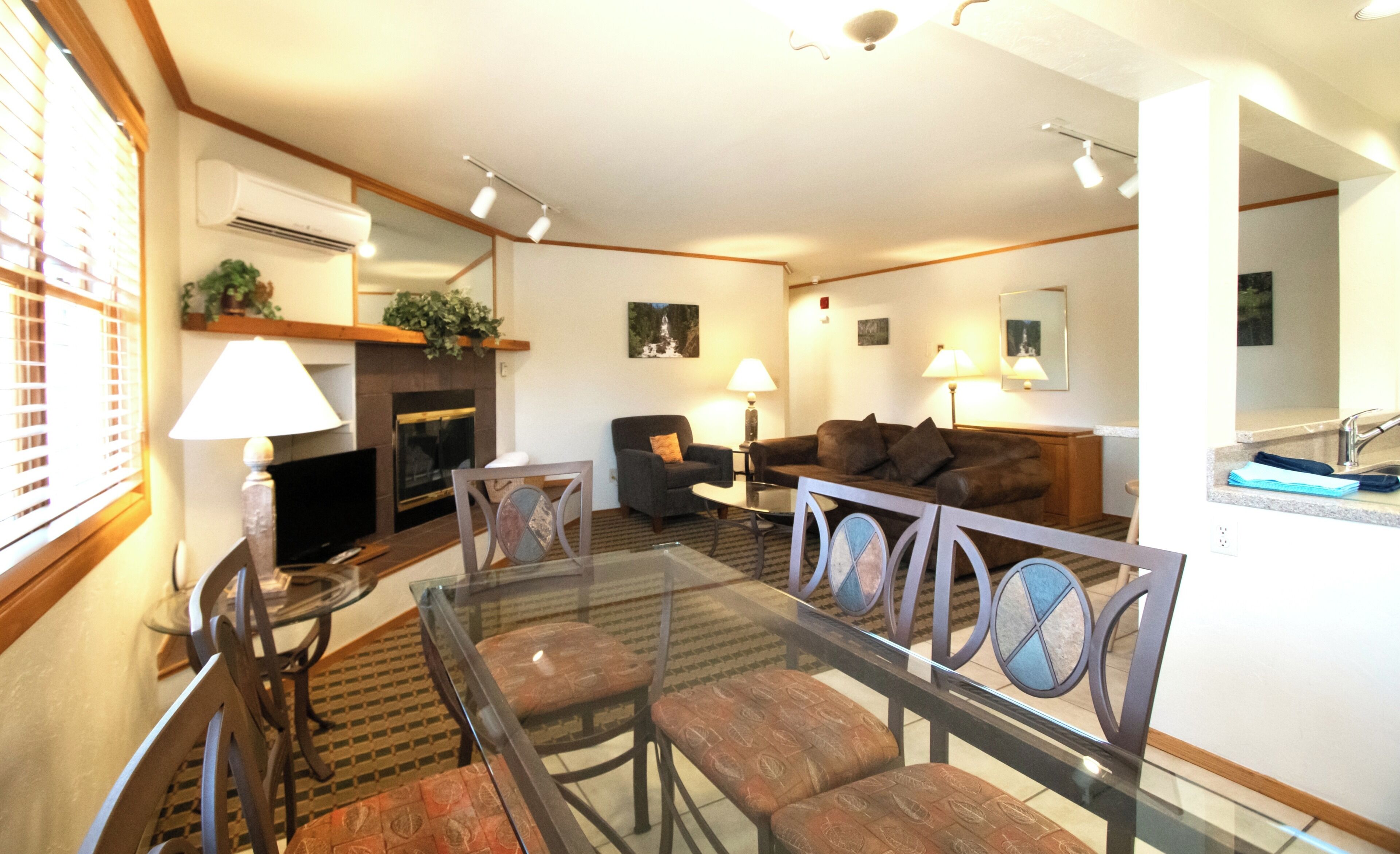 Una sala de estar con una mesa de centro de vidrio, dos sillones, un sofá, una chimenea y un comedor con sillas.