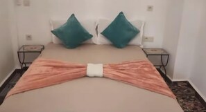 A bed with a pink blanket tied in a bow, two teal pillows, and a bedside table with a lamp. - Beautiful riad in the city center (Marrakesh)