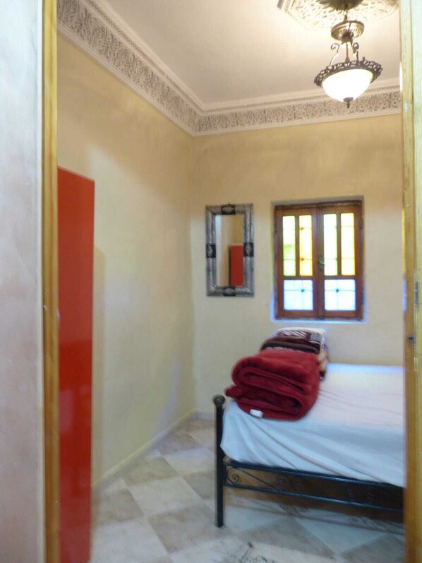 A bedroom with a bed, a window with blinds, a mirror, and a ceiling light fixture.