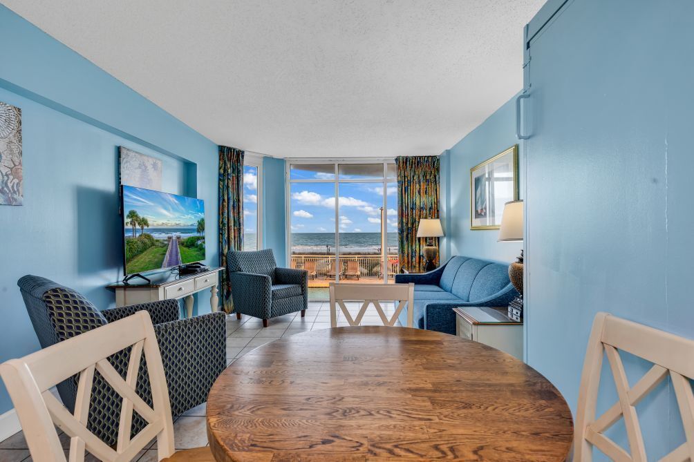 A room with a large window, a wooden dining table, two sofas, and a television.