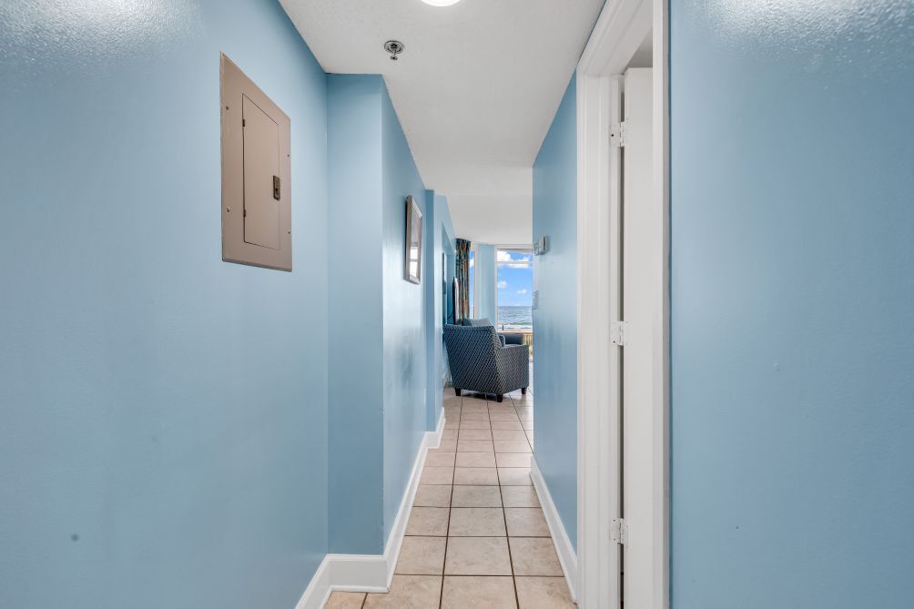 A hallway with light blue walls, a tiled floor, and a door on the right.
