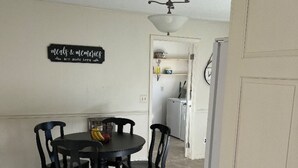 Ein Essbereich mit einem runden Tisch, vier Stühlen, einem Deckenventilator und einer im Hintergrund sichtbaren Küche.