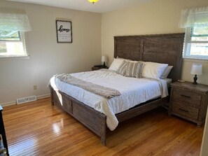 A bedroom with a wooden bed, a nightstand, a wall-mounted lamp, and a framed 'home' sign.