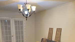 Ein Wohnzimmer mit grauem Sofa, einem gemusterten Teppich, einer Kristallleuchtre und zwei Wandpaneelen.