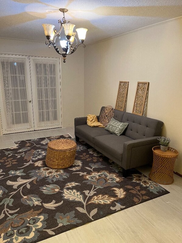 A living room with a grey sofa, a patterned rug, a chandelier, and two decorative panels on the wall.