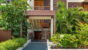 A modern two-story building with a covered entrance, outdoor seating, and lush tropical vegetation.
