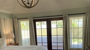 A spacious bedroom with a large bed, a chandelier, and a view of a wooden deck through a sliding glass door. - Close to Village & Pier, quiet retreat, bunk room  with toys, games, books & TV (St. Simons Island)