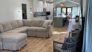 A spacious living area with a large L-shaped sectional sofa, a dining table with chairs, and a kitchen in the background. - Close to Village & Pier, quiet retreat, bunk room  with toys, games, books & TV (St. Simons Island)