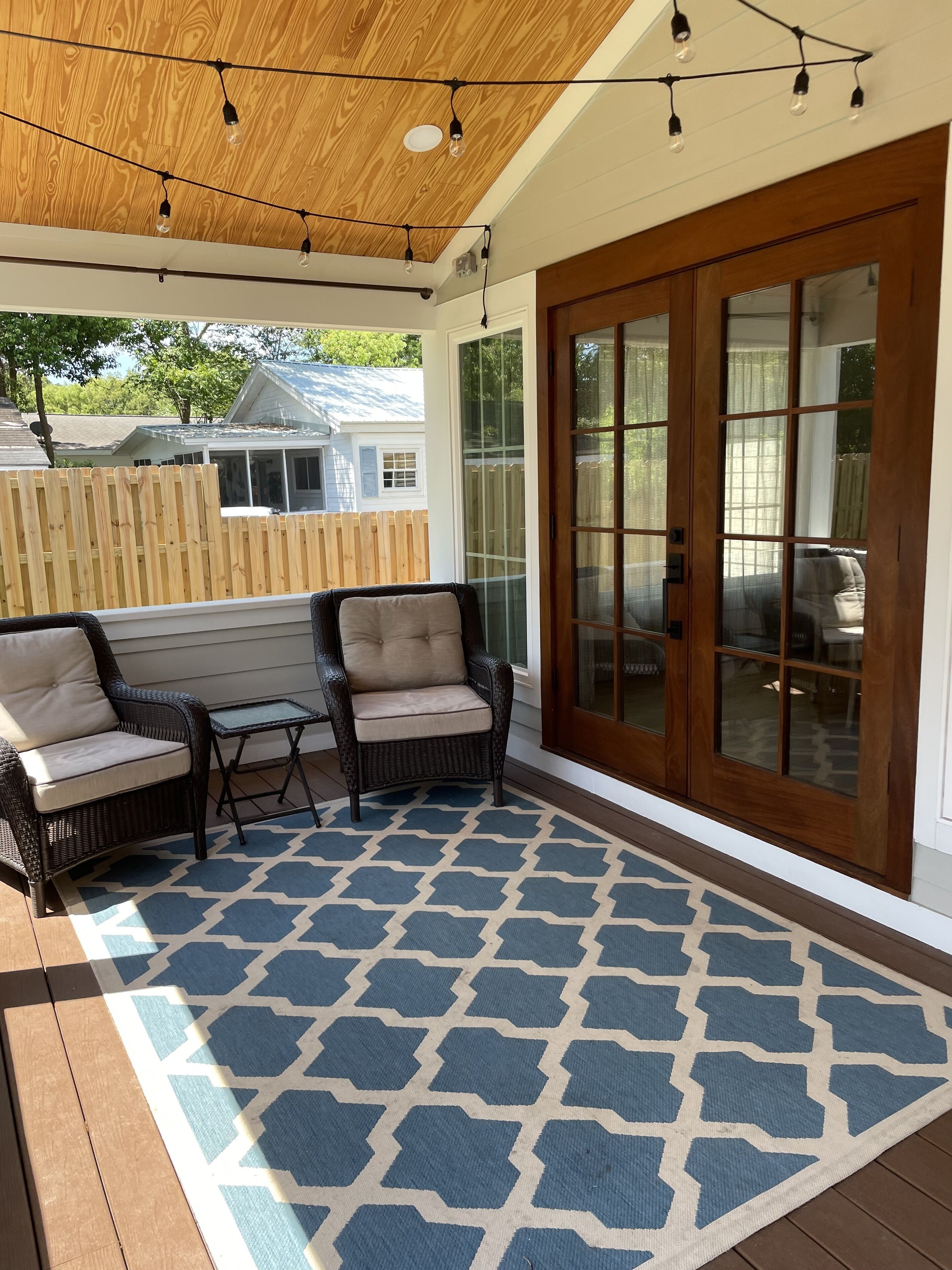 Un patio couvert aménagé avec des meubles en osier, un tapis à motifs et une porte-fenêtre coulissante.
