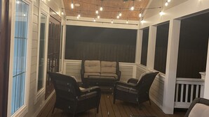 A covered porch with wicker furniture, string lights, and a ceiling fan. - Close to Village & Pier, quiet retreat, bunk room  with toys, games, books & TV (St. Simons Island)