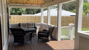 A covered outdoor patio with wooden flooring, black wicker furniture, and string lights. - Close to Village & Pier, quiet retreat, bunk room  with toys, games, books & TV (St. Simons Island)