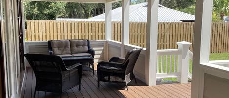 A covered outdoor patio with wooden flooring, black wicker furniture, and string lights.