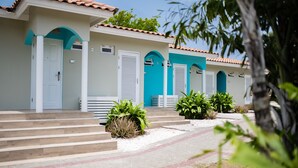 A row of hotel rooms with white walls and blue accents, featuring a tiled roof and a small garden area with plants. - Blue Bay Preferred Studio (Willemstad)