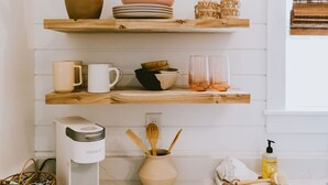 A kitchen with white wooden shelves, a coffee maker, a plant, and various kitchen items. - Canal front, Modern Tiny House! Bikes. Fire pit! (Kitty Hawk)