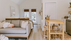 A cozy living room with a sofa, a wooden table with glasses, and a kitchen area with a dishwasher. - Canal front, Modern Tiny House! Bikes. Fire pit! (Kitty Hawk)