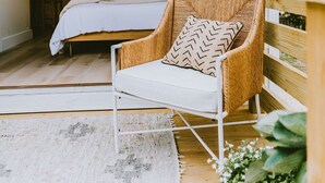 A bedroom with a bed, a wicker chair, a white rug, and a wooden floor. - Canal front, Modern Tiny House! Bikes. Fire pit! (Kitty Hawk)