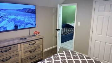 A room with a television on a wooden dresser, a patterned rug, a door leading to a bedroom, and a white door.