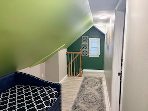 A hallway with a wooden staircase, a patterned rug, and a door leading to a room with green walls. - Spacious 3BR Home | Recently Remodeled | Private Yard & Parking (West Seneca)